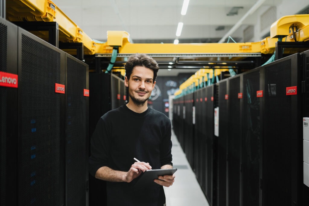 Junger Mann in Serverraum mit Tablet zwischen Servern und IT-Infrastruktur.