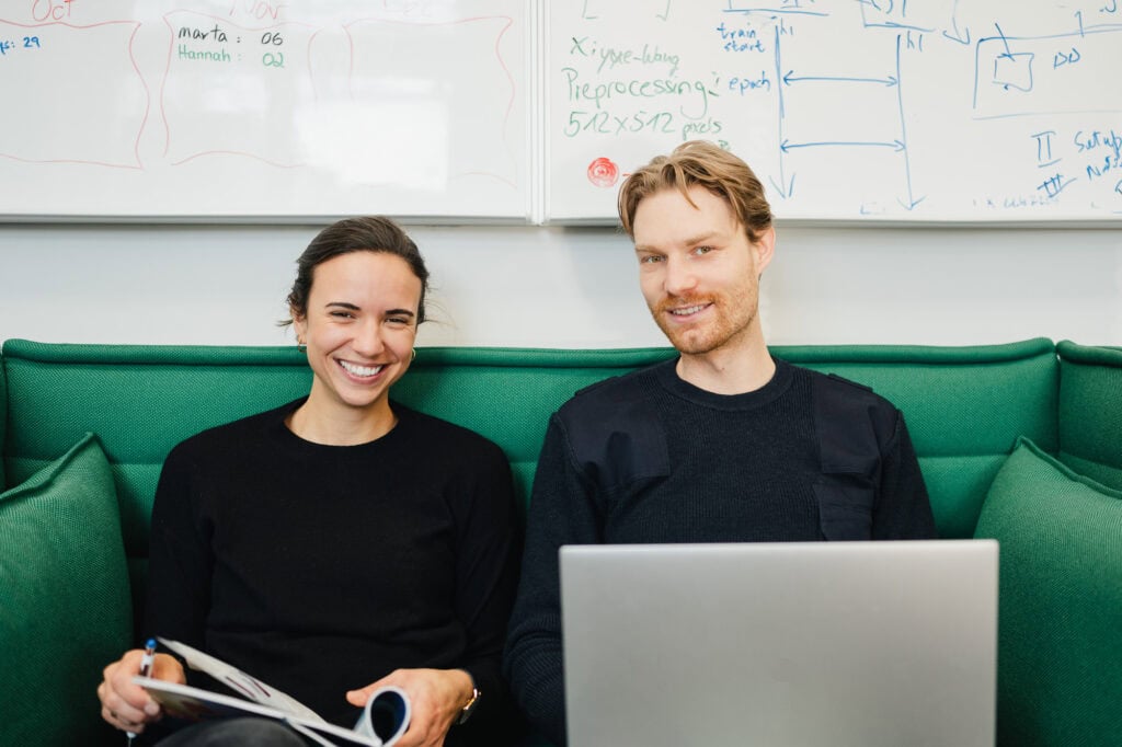 AI made in Germany: Ein zukunftsweisender Bildpool für die Konrad Zuse Schools (DAAD) 19 Zwei junge Menschen arbeiten in einem modernen Büro mit Whiteboard im Hintergrund.