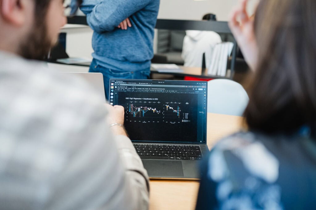 AI made in Germany: Ein zukunftsweisender Bildpool für die Konrad Zuse Schools (DAAD) 21 Menschen bei einer Finanzanalyse mit Laptop in einem Büro.