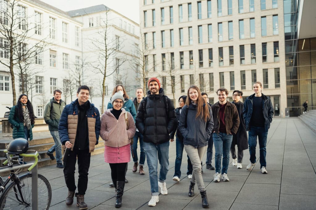 AI made in Germany: Ein zukunftsweisender Bildpool für die Konrad Zuse Schools (DAAD) 9 Junge Menschen beim Spaziergang in der Stadt vor modernen Gebäuden.