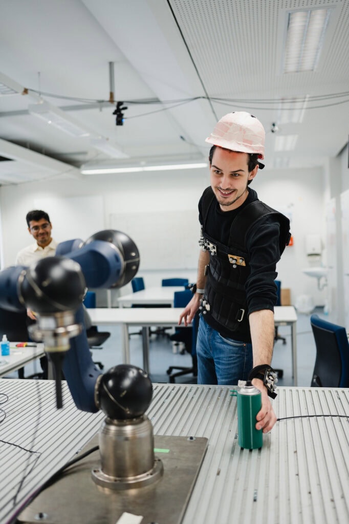 Junger Mann in Schutzhelm bedient Roboterarm in Techniklabor.