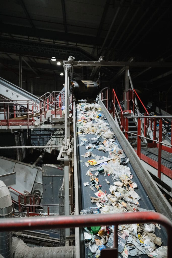 Recyclinganlage mit M&uuml;ll auf F&ouml;rderband in Industriehalle.
